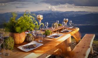 A beautifully set table on a mountain with a view of the mountains in the background. The table decoration includes plants, glasses, and nature-inspired elements.