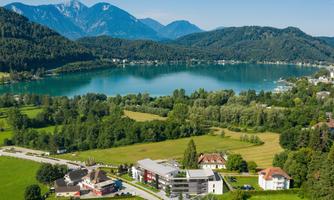 A picturesque landscape with a lake, surrounded by mountains and lush greenery. In the foreground, there are some buildings and fields visible.