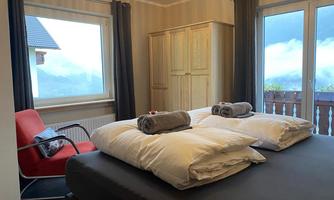 A cozy bedroom with two beds and fresh towels. The room has large windows with a view of the mountains and a red chair for relaxation.