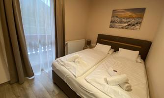 A cozy bedroom with two single beds and wooden flooring. Large windows let in plenty of light and offer a view of the surroundings.