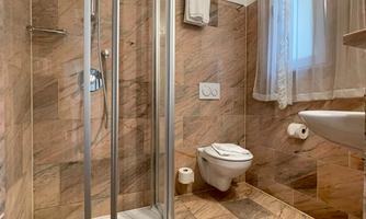 A modern bathroom with a shower and a toilet. The walls are decorated with gray tiles.