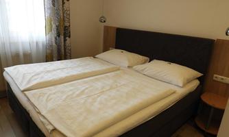 A cozy bedroom with a double bed and bright bed covers. In front of the window, a curtain allows sunlight in.