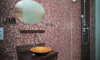 A modern bathroom with glazed tiles in brown tones. It features an elegant sink and a shower.
