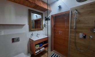 A modern bathroom with a shower, a sink, and a large mirror. The floor is covered with a striped mat and the walls are designed in light colors.