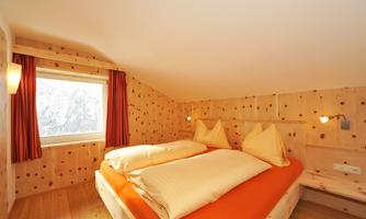 A cozy bedroom with a double bed and two decorative pillows. The walls are made of wood, and a window lets in natural light.
