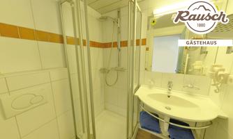 A bright bathroom with a walk-in shower and a modern sink. Orange tiles are visible on the wall, and there are white towels on a shelf.