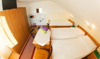 A cozy room with three beds and a table. There is a wardrobe and a sink in the room, as well as towels in various colors.