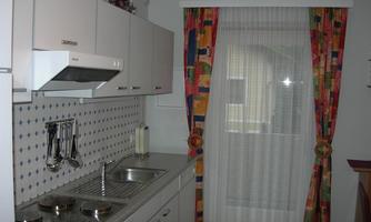 A modern kitchen with bright cabinets and a central sink. The windows are adorned with colorful curtains.