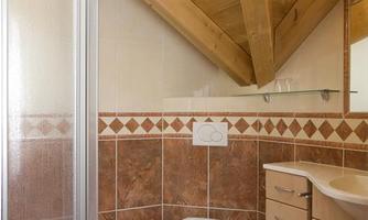 A modern bathroom with a shower cabin and sloping wooden ceilings. There is a bright color scheme and practical furniture.