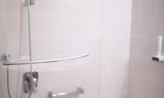 A modern bathroom with a bathtub and a glass sliding door. The walls are light tiled and decorated with blue accents.