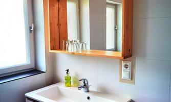 A modern bathroom with a sink and a wooden mirror. Natural light comes through the window.