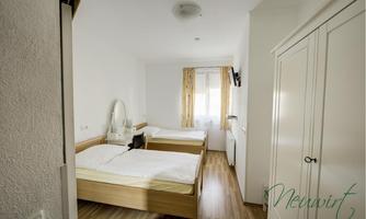 A simple room with two single beds and a large window. The room has light walls and a modern wardrobe.
