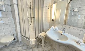 A bright bathroom with a shower and a sink. The walls are tiled and the space feels clean and modern.