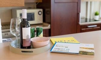 A table with a bottle of red wine, glasses, and drink cans. Next to the wine are snacks and some books.