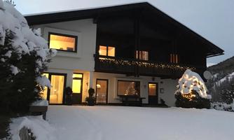 A modern house in the snow, illuminated with warm light. The surroundings are wintry and peaceful.