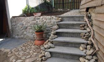 A garden area with a stone step path that leads to a paved area. On the right, there is wood cladding and a boundary made of stones.