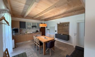 A modern kitchen with a large dining table and wooden ceilings. The space is bright and friendly designed.