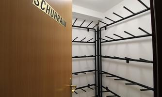 A shoe room with an open door. Black shelves for placing shoes are mounted on the walls.