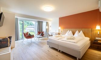 A modern hotel room with a large double bed and a cozy seating area. Large windows let in plenty of light and offer a view of nature.