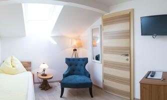 A cozy room with a blue armchair, a lamp, and a wooden sofa. The room has a skylight that lets in plenty of daylight.