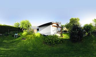 A well-kept garden with green grass and trees. In the background stands a cozy house.