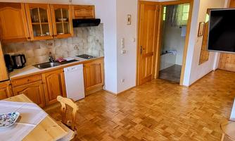 A bright kitchen with wooden cabinets and a dining area. In the background, a bathroom can be seen.
