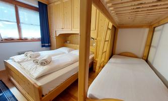 A cozy bedroom with a double bed and a bunk bed. The wood paneling and the windows create a warm atmosphere.