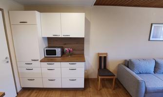 A modern kitchen with white cabinets and a microwave. In the background, there is a gray sofa and a chair.