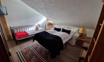 A cozy room with a double bed and a single bed. The decor is simple and inviting, with a rug and natural light.