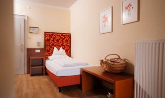 A cozy room with a single bed, a table, and a basket. The walls are in soft colors and there are decorative pictures.