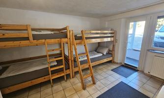 A simple room with two wooden bunk beds. The room has a tiled floor and access to the outside.