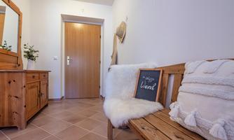An inviting hallway with a wooden bench and a mirror. The walls are light, and a sign reading "Welcome" hangs on the bench.