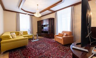 A cozy living space with a yellow sofa, a brown armchair, and a large rug. Large windows let in plenty of light and create an inviting atmosphere.
