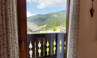 A window with a view of green hills and a clear blue sky. The curtains are open, letting light in.