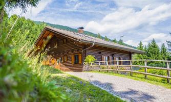 A charming wooden house in nature, surrounded by trees and a clear sky. The path has a lovely stone street and a fence enclosure.