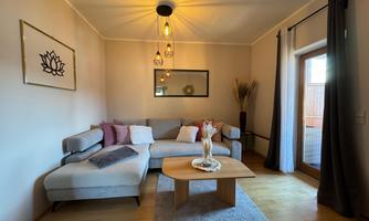 A stylish living room with a gray sofa and modern decor. Large windows provide plenty of daylight and a cozy atmosphere.