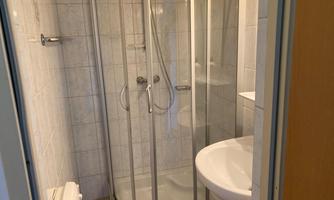 A small bathroom with a shower, a sink, and a toilet. The walls are adorned with light tiles.