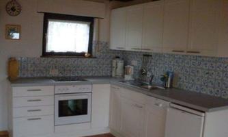 A modern kitchen with white furniture and blue tiles on the wall. There is a stove, a sink, and plenty of storage space.