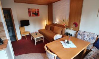 A cozy living space with a sofa, table, and chairs. Pictures hang on the wall and there are flower vases on the table.