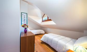 A cozy room with slanted walls and two single beds. On the nightstand, there is a vase with colorful flowers.