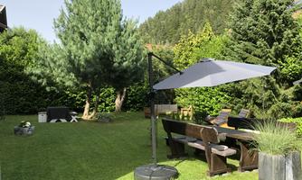 A beautiful garden with a large terrace and a sun umbrella. Surrounded by green trees, the space offers an inviting place to relax.
