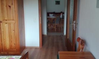 A cozy room with wooden furniture and a small table. In the background, there is an open door leading to another room.