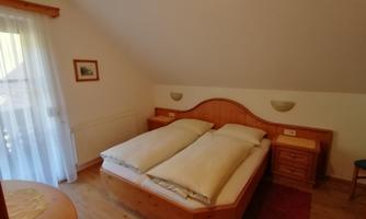 A cozy bedroom with a large double bed and wooden furniture. The room has a warm atmosphere and a view of the balcony.