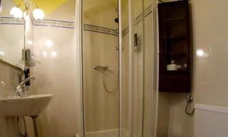 A small bathroom with a shower cubicle, toilet, and basin. The walls are light-tiled and the ceiling has a yellow color.