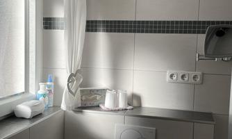 A bright bathroom with a window and modern tiled cladding. On the shelf are placed care products and towels.