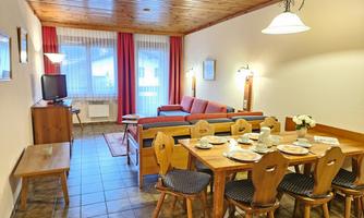A cozy living area with a dining area and a couch. Large windows provide plenty of daylight.