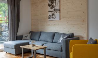 A modern living room with a gray sofa and a yellow armchair. The wooden floor and wood paneling give the room a cozy atmosphere.