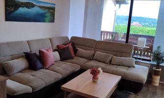 A modern living room with a comfortable sofa and a wooden table. Large windows provide a view of the landscape.