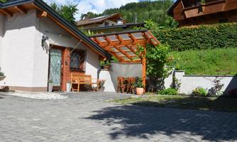 A cozy house with a terrace and wooden furniture. Surrounded by green hills and a clear sky.