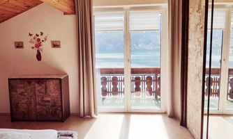 A cozy bedroom with a balcony view of a lake. Large windows let in plenty of daylight and create an inviting atmosphere.